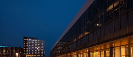 A modern hotel with a glass facade, a spacious lobby, and a parking area.