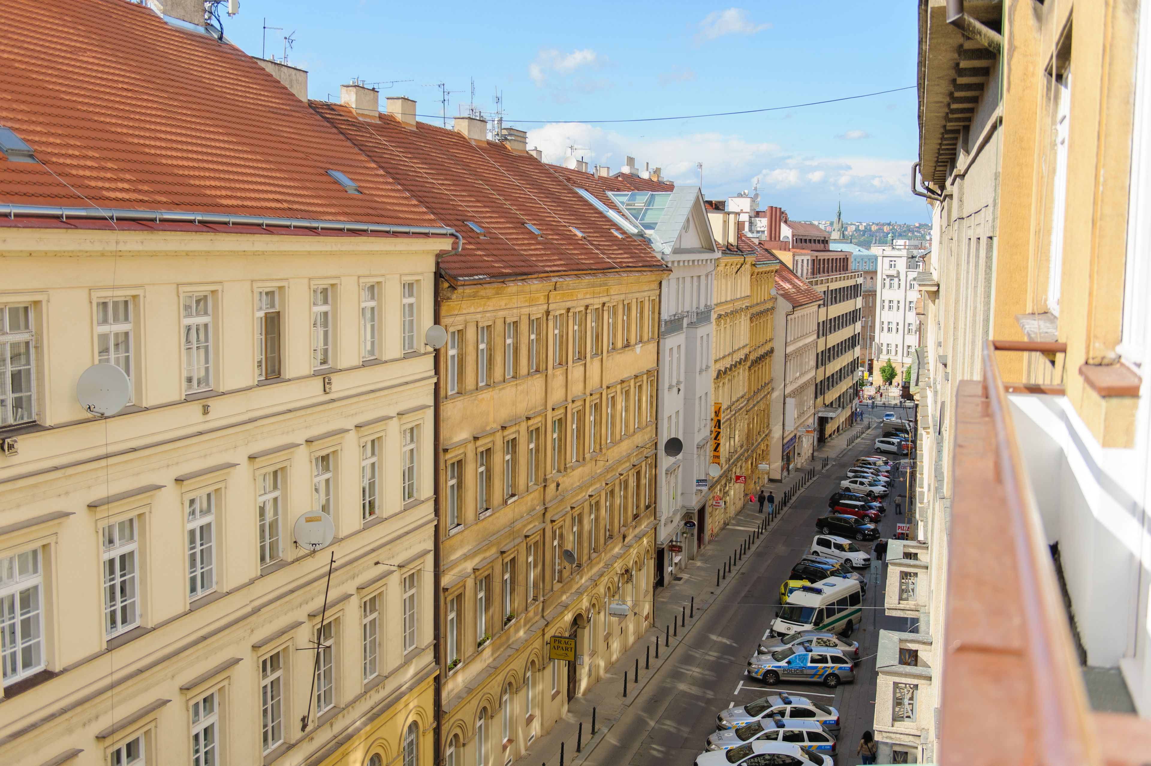 A street view of a city with historic buildings, a clear sky, and parked cars along the sidewalk.