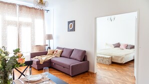 A modern living room with a sofa, dining table set for two, and a bedroom with a bed and nightstand. - Stunning Design Apartment (Prague)