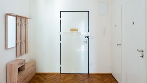 A room with a wooden cabinet, a white door with a glass panel, and a herringbone-patterned floor. - Stunning Design Apartment (Prague)