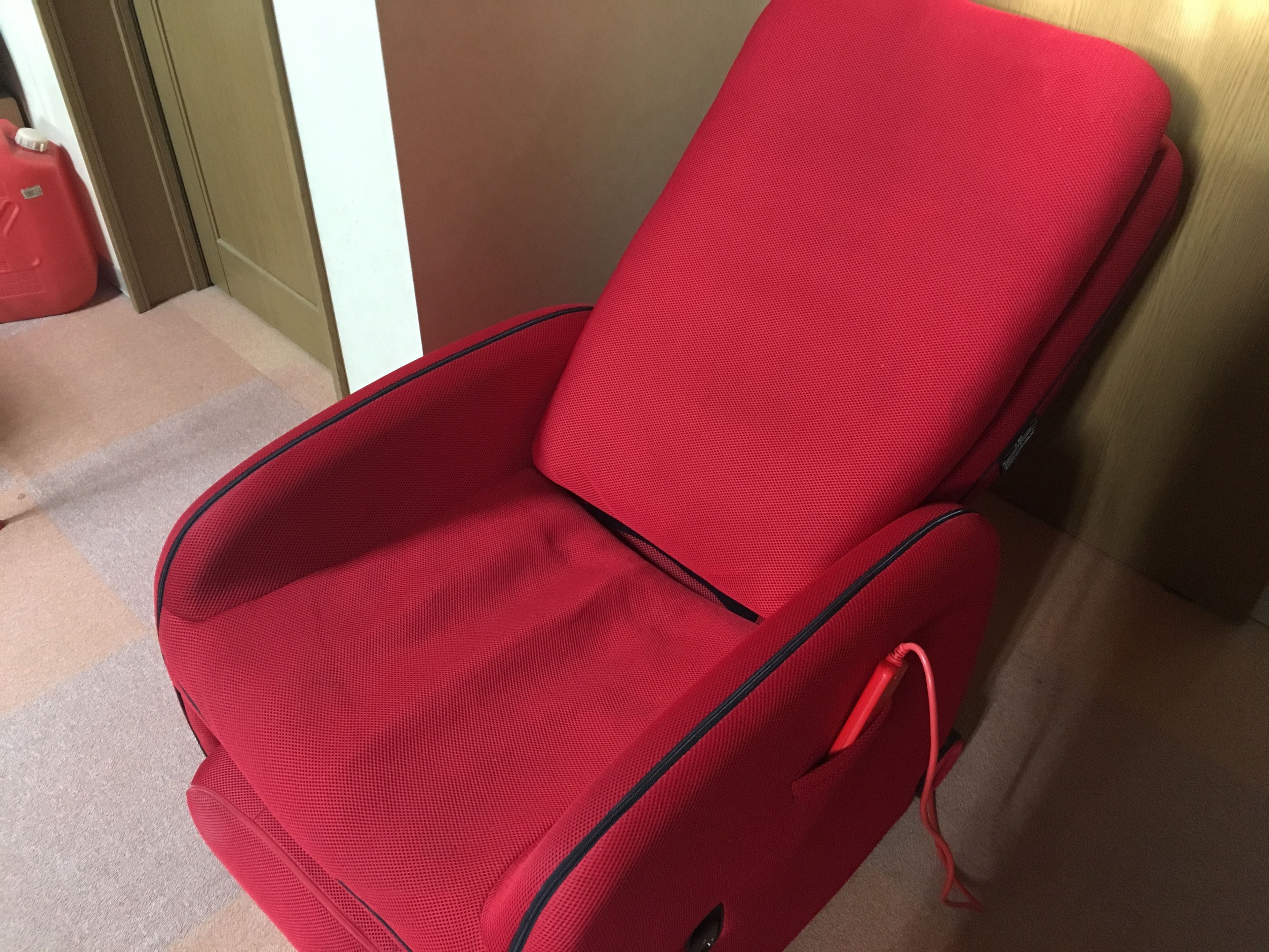 Een rode stoel met een zwart frame, geplaatst in een kamer met een beigekleurig tapijt en een witte deur op de achtergrond.