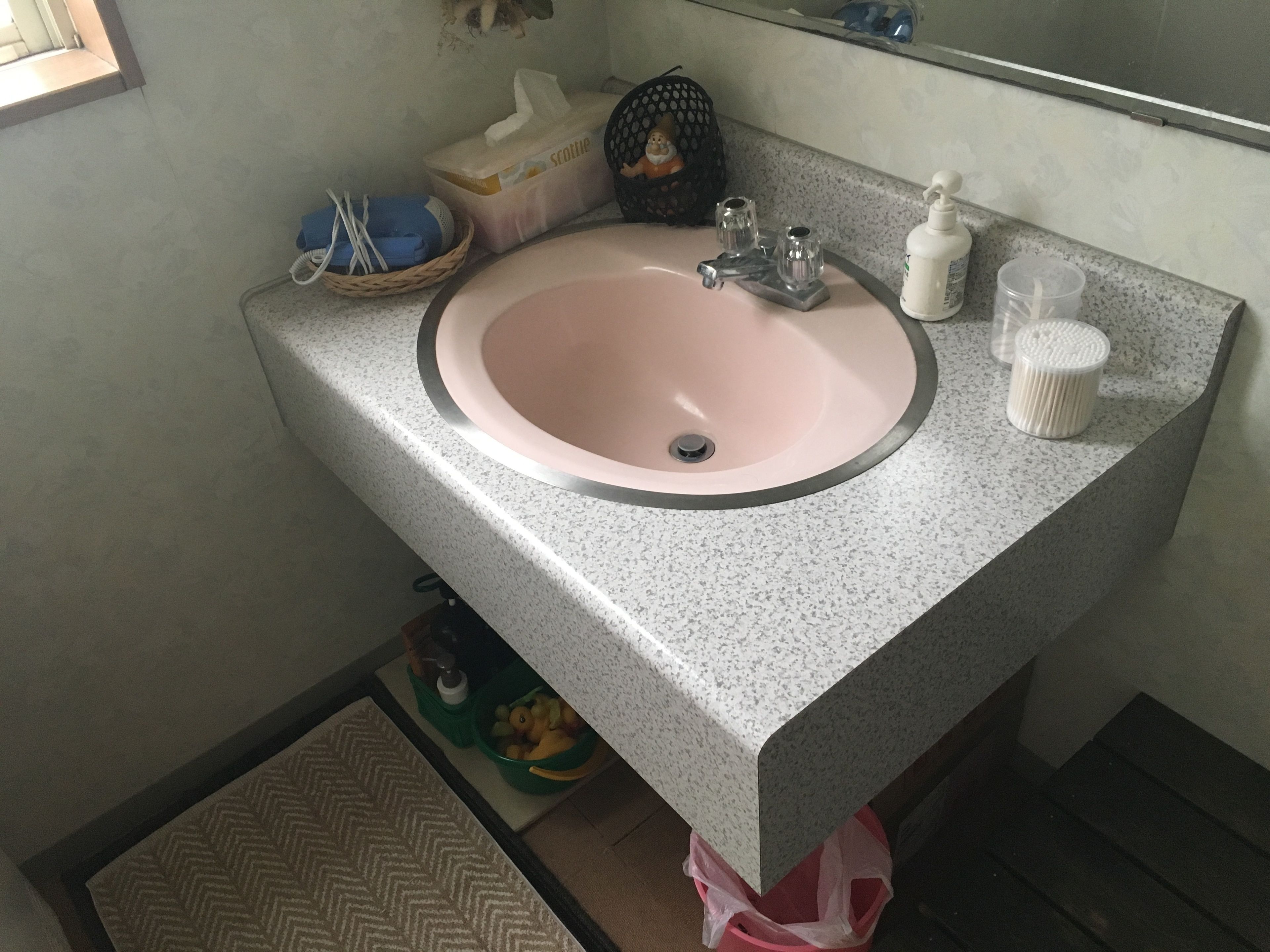A bathroom with a pink sink, a mirror, and various toiletries on the countertop.