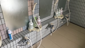 A bathroom with multiple showerheads, a hand dryer, and personal care products on a shelf.