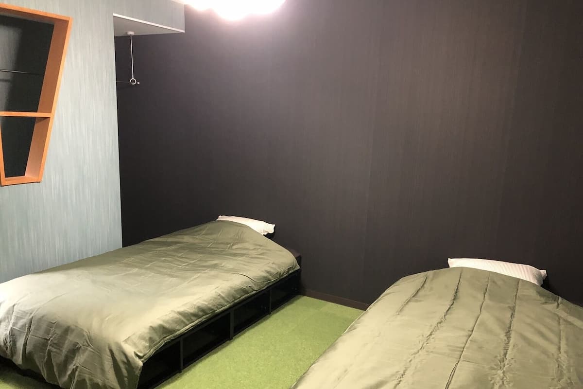 Ein Zimmer mit zwei Einzelbetten, einem kleinen Fenster und einer Lampe.