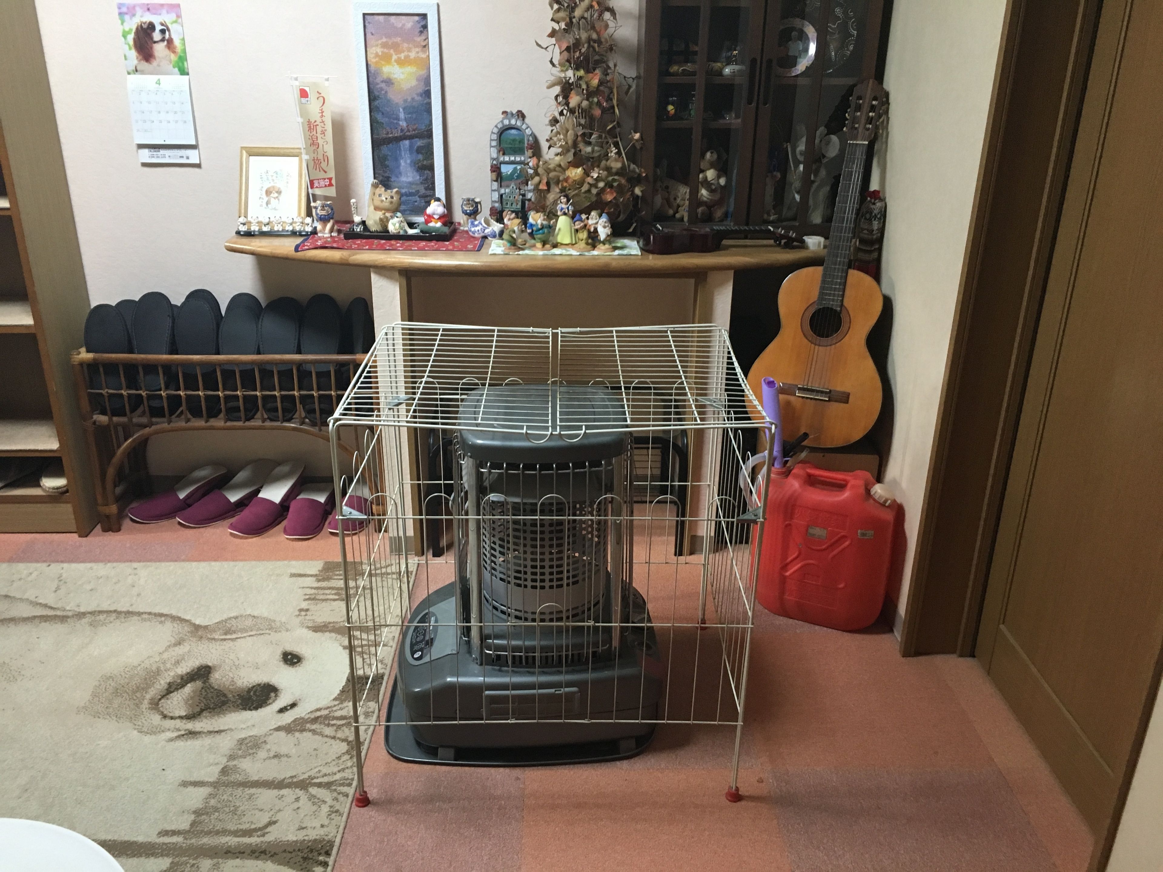 A room with a heater in a cage, a guitar, and a cabinet with various items.