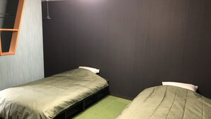 A small, dimly lit room with two single beds, a window with a wooden frame, and a green carpet.