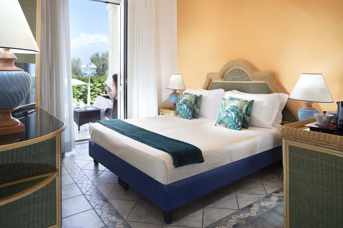 A hotel room with a large bed, two bedside tables, a view of the outdoors, and a balcony.