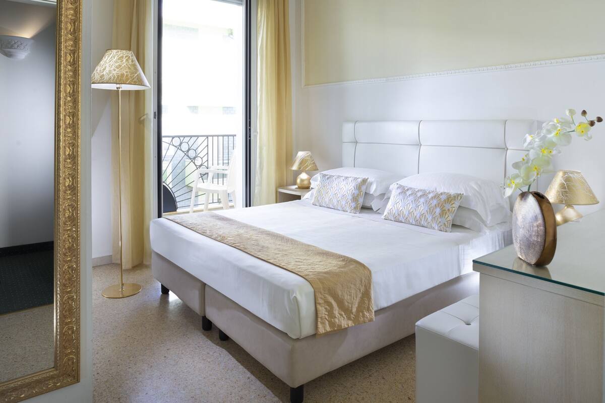 A hotel room with a large bed, two bedside tables, a mirror, and a view of the outside balcony.