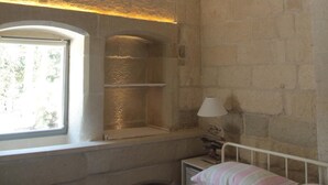 A bedroom with a stone wall, a window, a bed, and a nightstand.