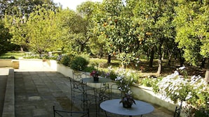 An outdoor patio with a round table and metal chairs, surrounded by lush greenery and flowering plants.
