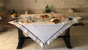A breakfast table set with bread, pastries, fruits, and beverages, with a rustic stone wall in the background.