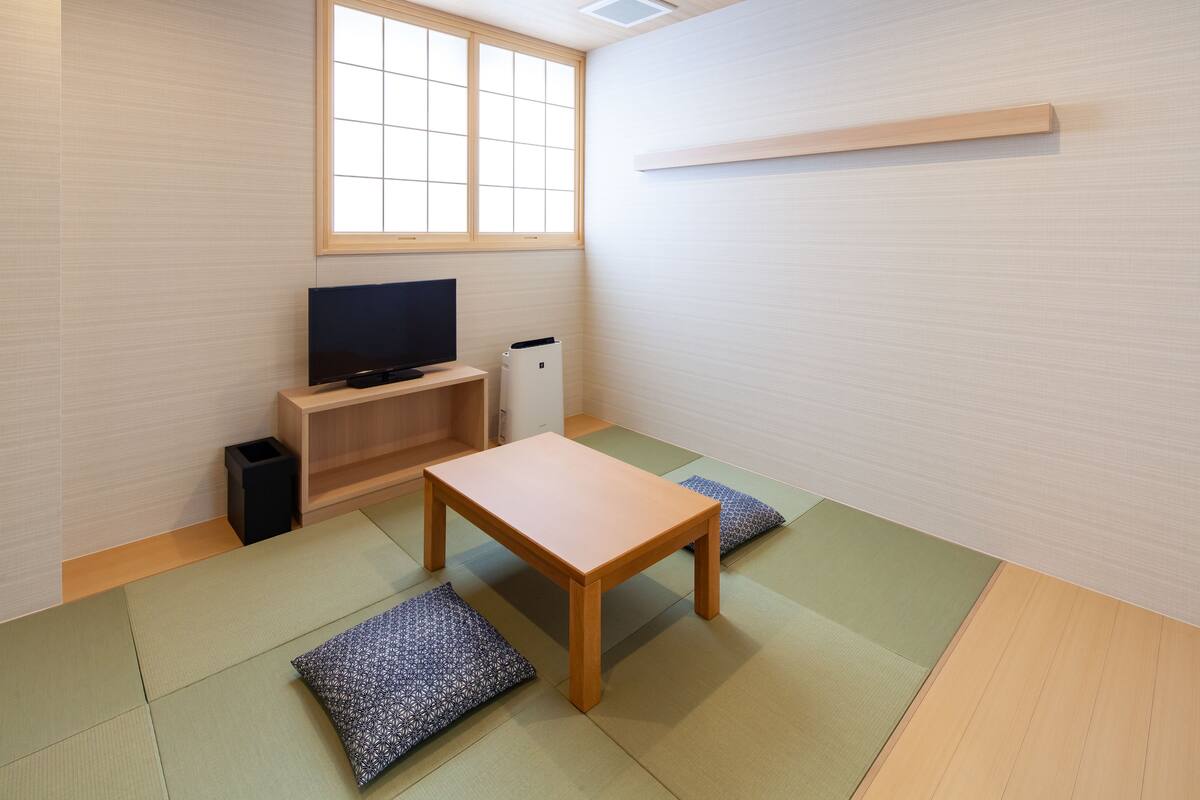 Una habitación con suelo de tatami, televisor, una mesita y ventana.