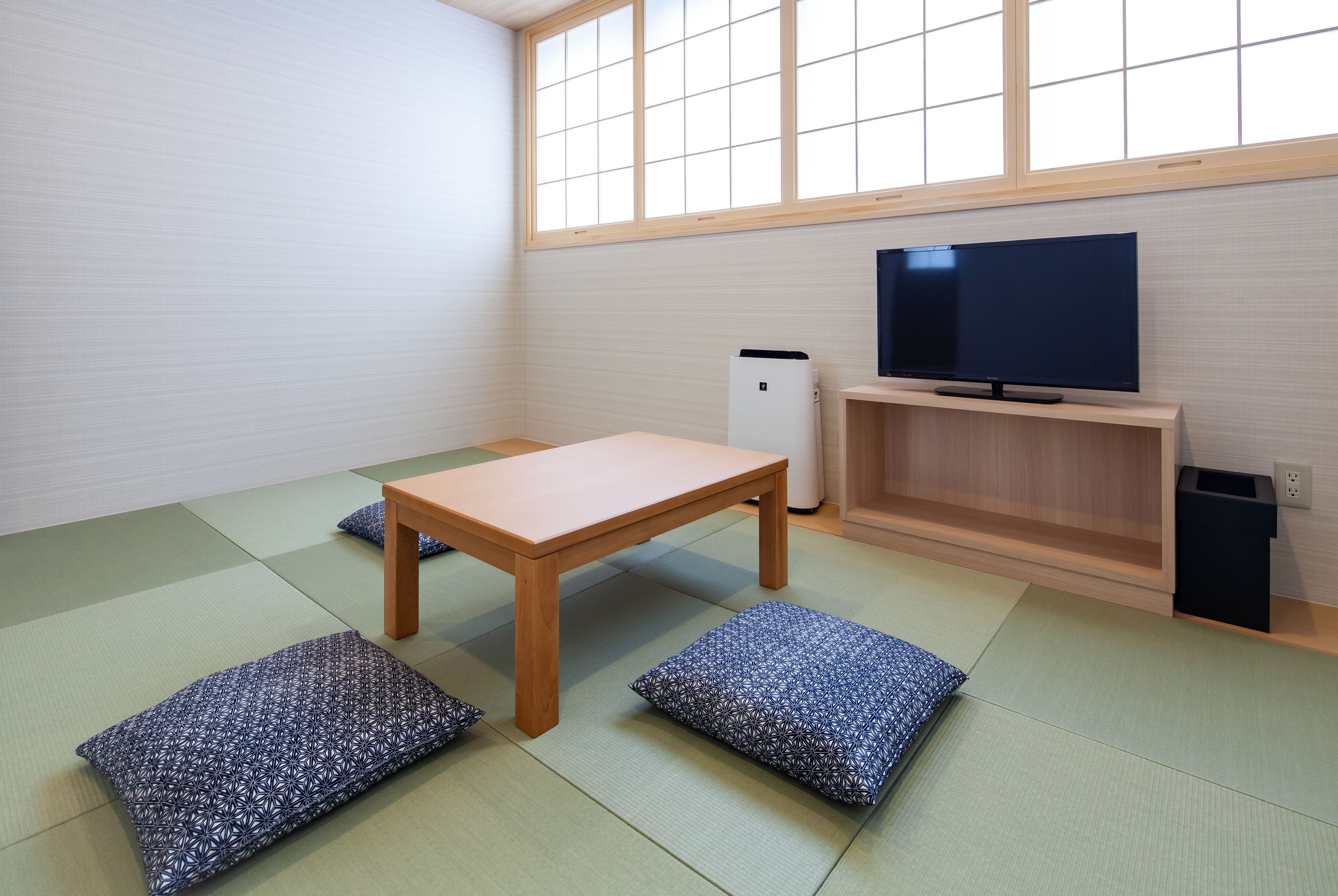 Een kamer met tatami vloerbedekking, een houten tafel, een televisie en een klein wit apparaat.