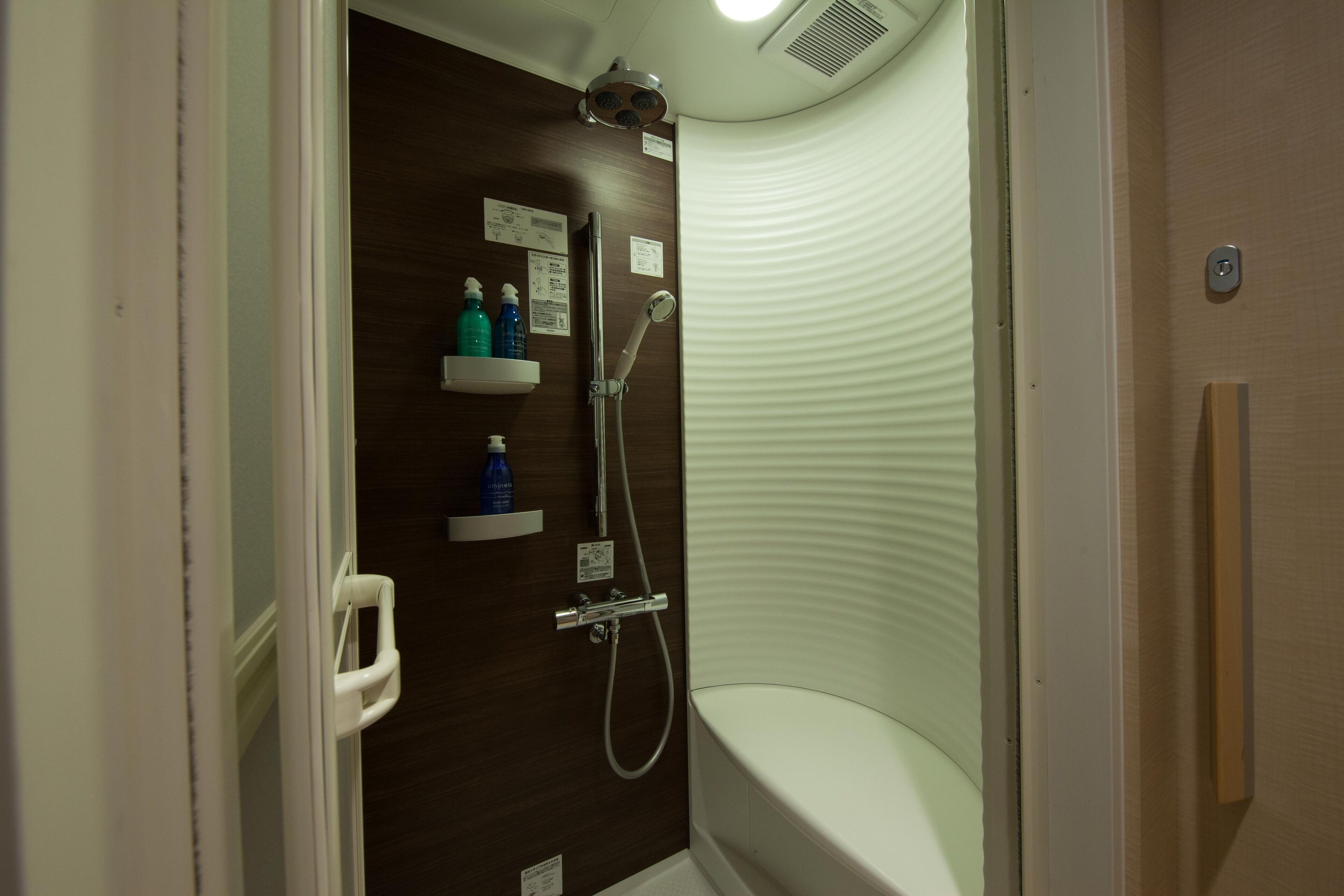 Un baño pequeño y moderno con ducha, inodoro y estante con artículos de aseo.