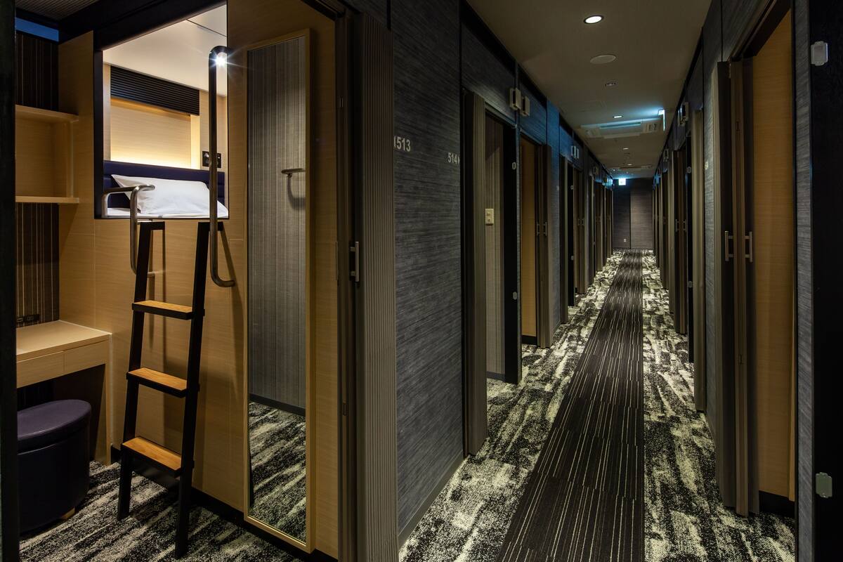 Un pasillo de hotel con piso alfombrado, puertas de madera y una escalera en una habitación.