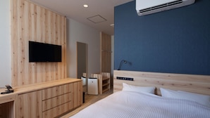 A modern hotel room with a wooden wardrobe, a flat-screen TV, a bed with white bedding, and an air conditioning unit on the wall. - Y's Cabin & Hotel Naha Kokusai Dori (Naha)