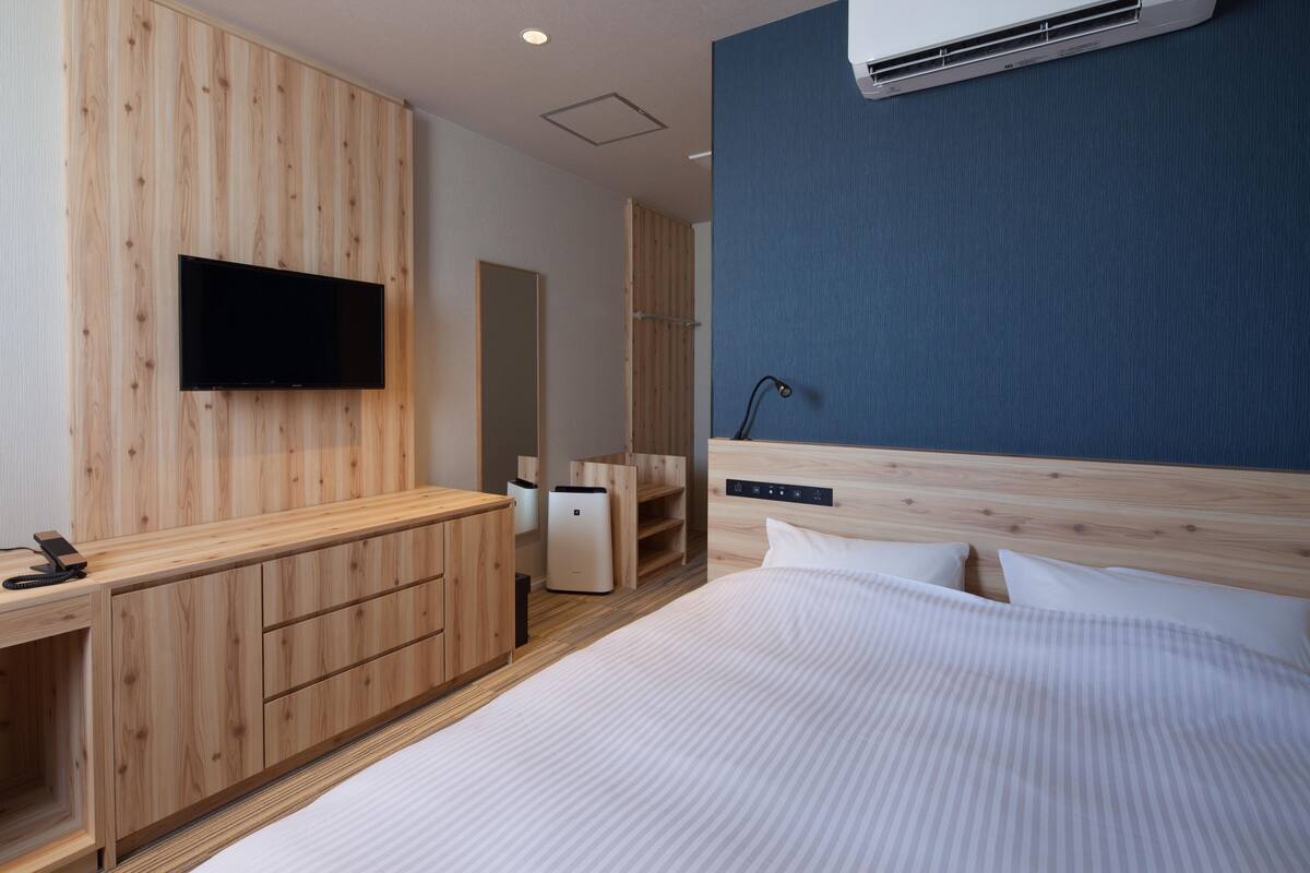 Una habitación de hotel moderna con un armario de madera, un televisor de pantalla plana, una cama con ropa blanca y un equipo de aire acondicionado en la pared.