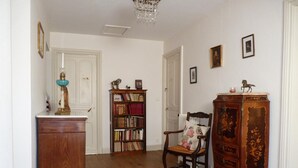 Een kamer met een houten vloer, een houten kast, een boekenkast, een stoel met een bloemenkussen en een decoratief houten object met een paardenbeeld.
