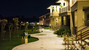 A well-lit hotel corridor with a curved pathway, outdoor plants, and a staircase leading to the upper floors. - Corbett The Baagh Spa & Resort (Ramnagar)