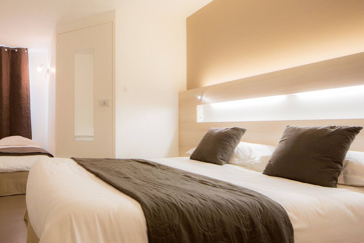 Habitación de hotel con cama, cabecero con iluminación integrada, una puerta y una cortina.