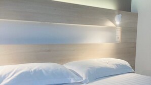 A neatly made bed with white linens and pillows, a wooden headboard, and a wall-mounted light fixture. - Hôtel Restaurant L’Eskemm *** St Brieuc-Trégueux (Tregueux)