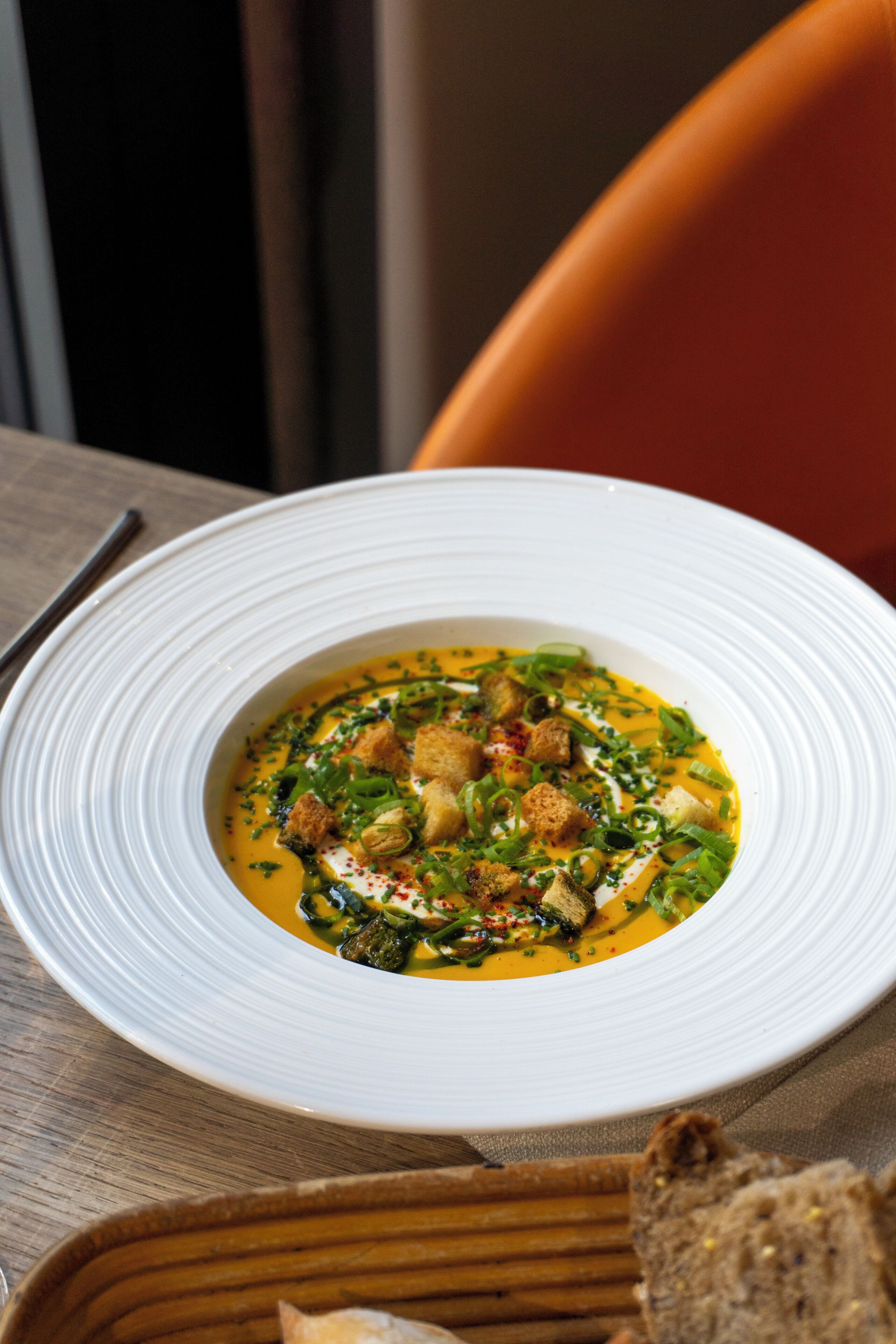 A white plate with a soup garnished with herbs and croutons, placed on a wooden table.
