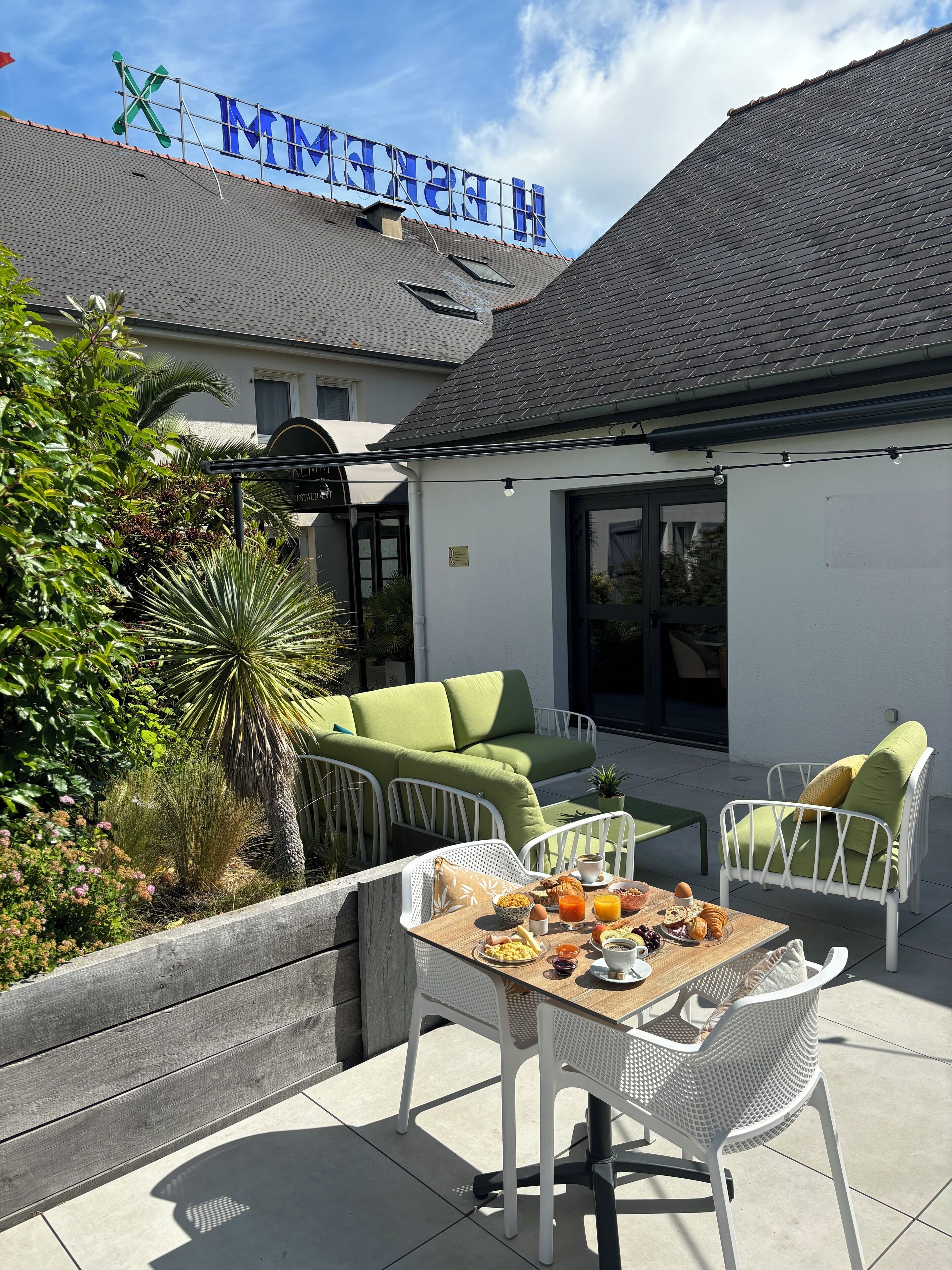 Une terrasse avec une table dressée pour le petit-déjeuner, des chaises en osier blanc et un canapé vert.