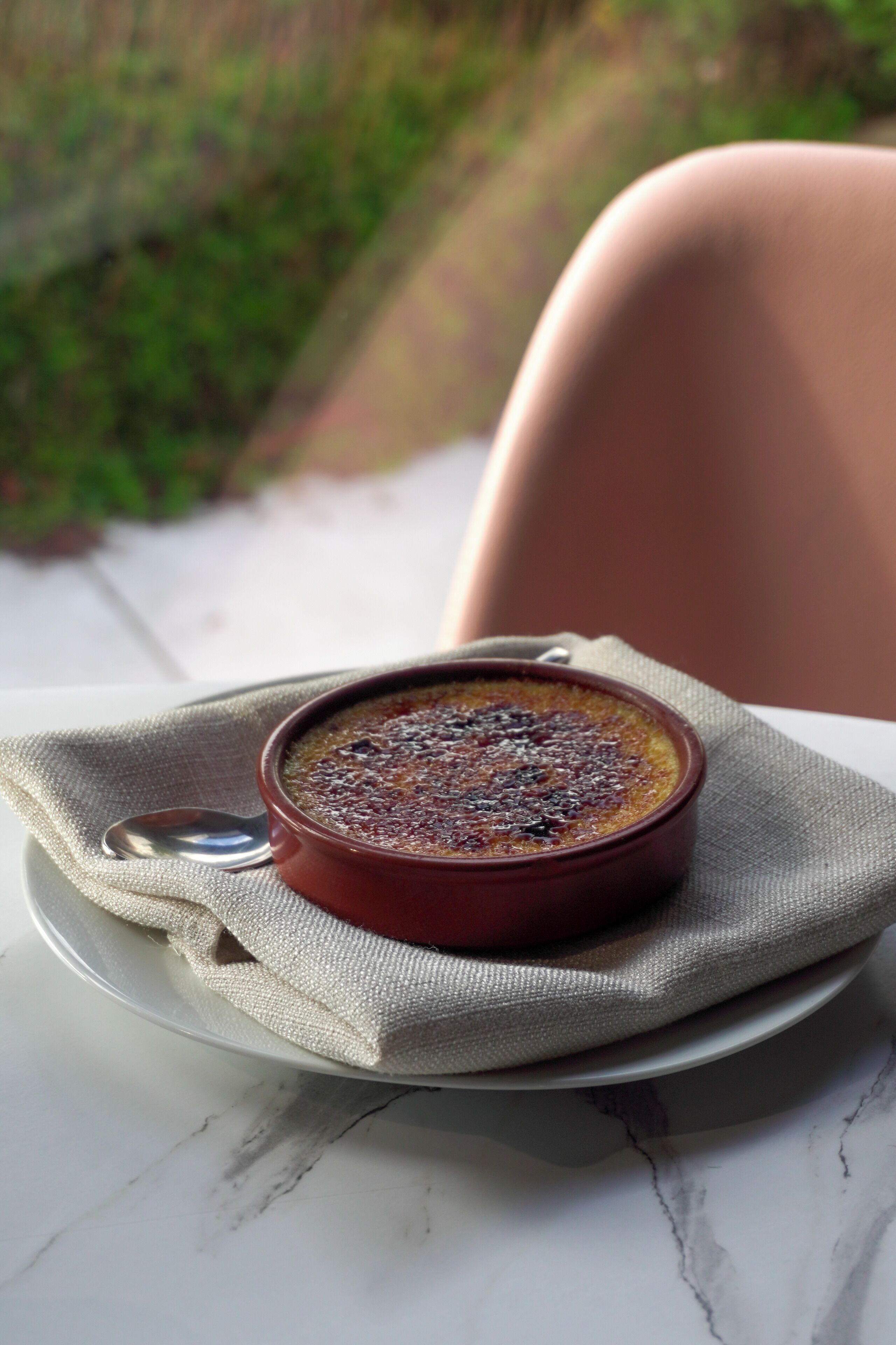 A dessert in a ceramic dish on a white plate, placed on a table with a beige cloth.