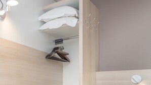 A modern, compact bedroom with built-in storage, a hanging rack, and a bedside table. - Hôtel Restaurant L’Eskemm *** St Brieuc-Trégueux (Tregueux)