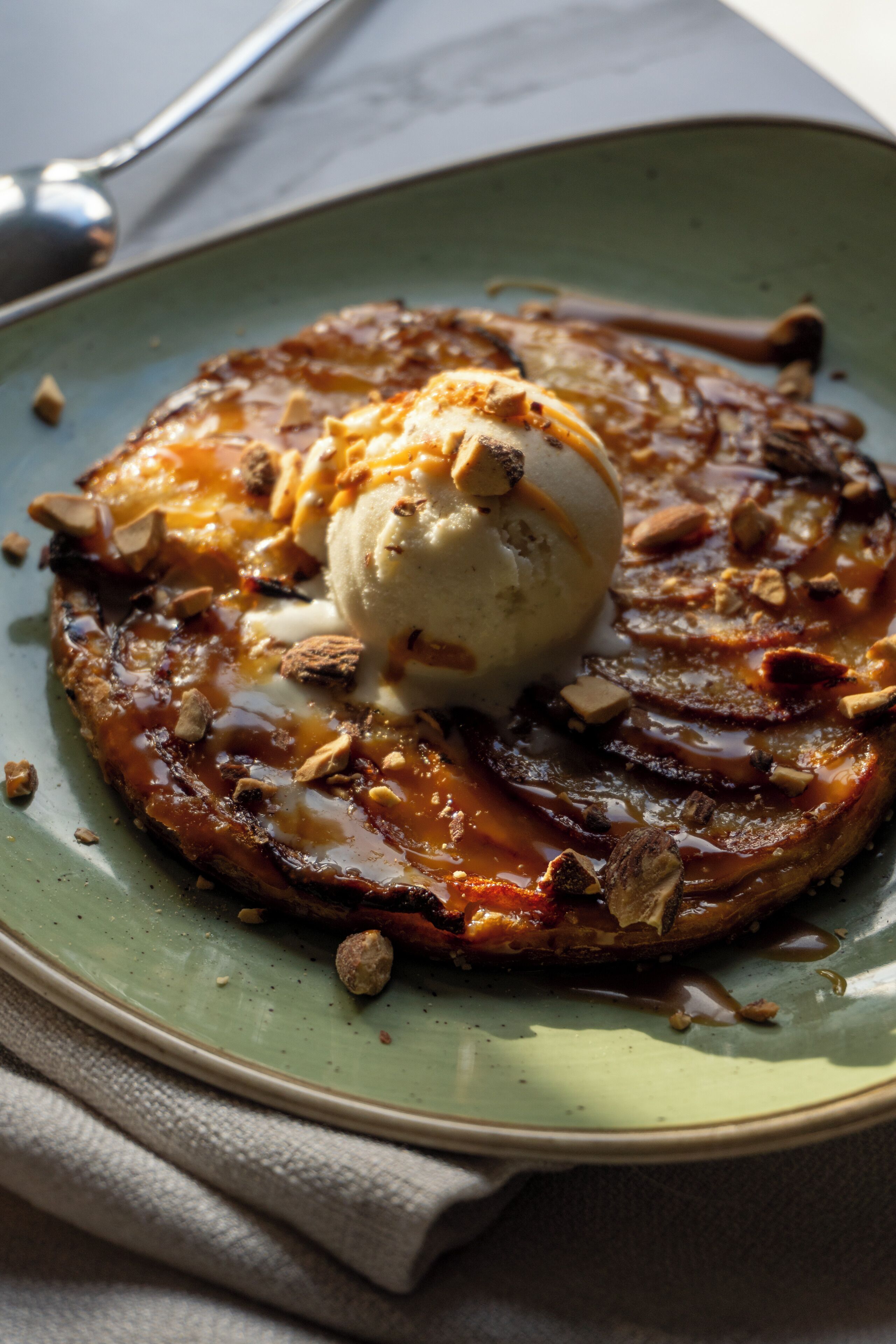 Un plato de postre con un pastel caramelizado, nueces y una bola de helado.