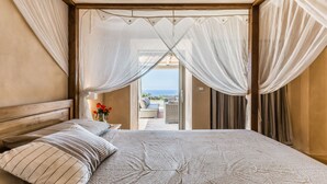 A bedroom with a large bed, a wooden headboard, and a view of the outdoors through a doorway. - Wp Relais Dammusi Posidonia (pantelleria)