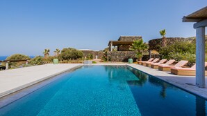 A pool with lounge chairs and a stone building with a view of the sea. - Wp Relais Dammusi Posidonia (pantelleria)