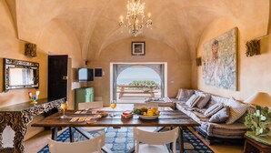 A dining area with a table set for two, a chandelier, and a view of the sea through an arched doorway. - Wp Relais Dammusi Posidonia (pantelleria)