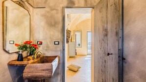 A bathroom with a wooden sink, a mirror, and a vase with red flowers. - Wp Relais Dammusi Posidonia (pantelleria)