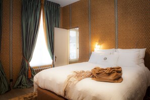 Habitación de hotel con una cama grande, una ventana con cortinas y un papel tapiz estampado.