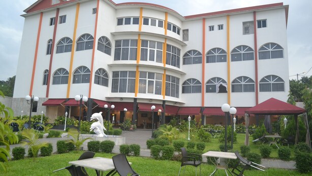 A multi-story building with a curved facade, large windows, and outdoor seating areas with tables and chairs. - Le Jardin d'eden 2 (Abidjan)