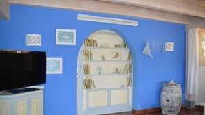 Um quarto com parede azul, uma estante de livros, uma televisão sobre um móvel e um barril.