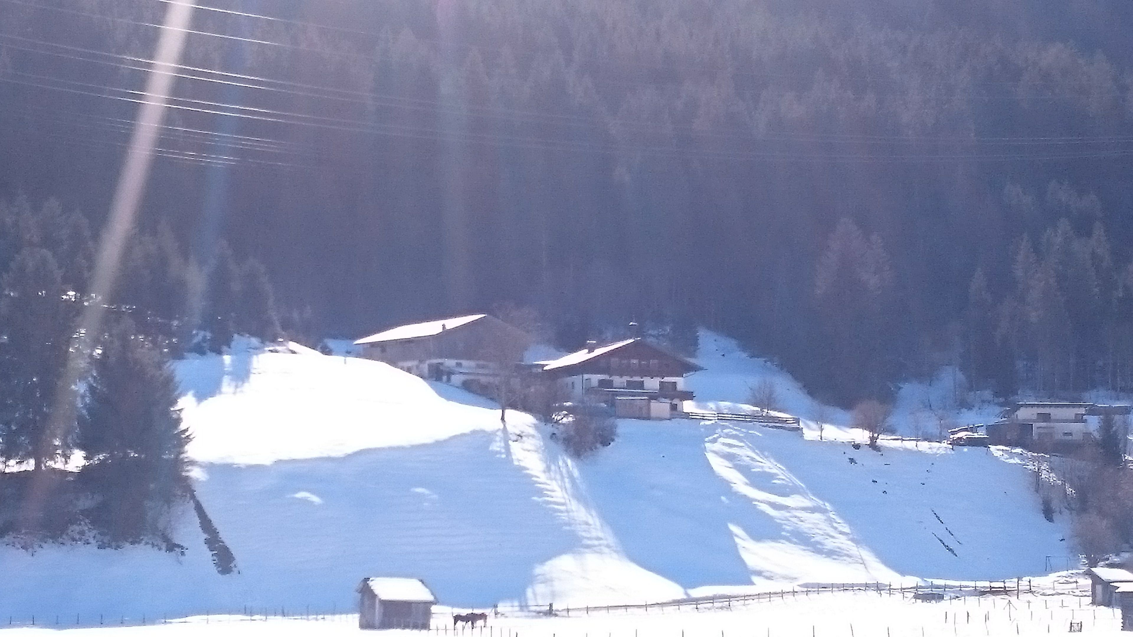 A snow-covered mountain with a few buildings and a ski slope.
