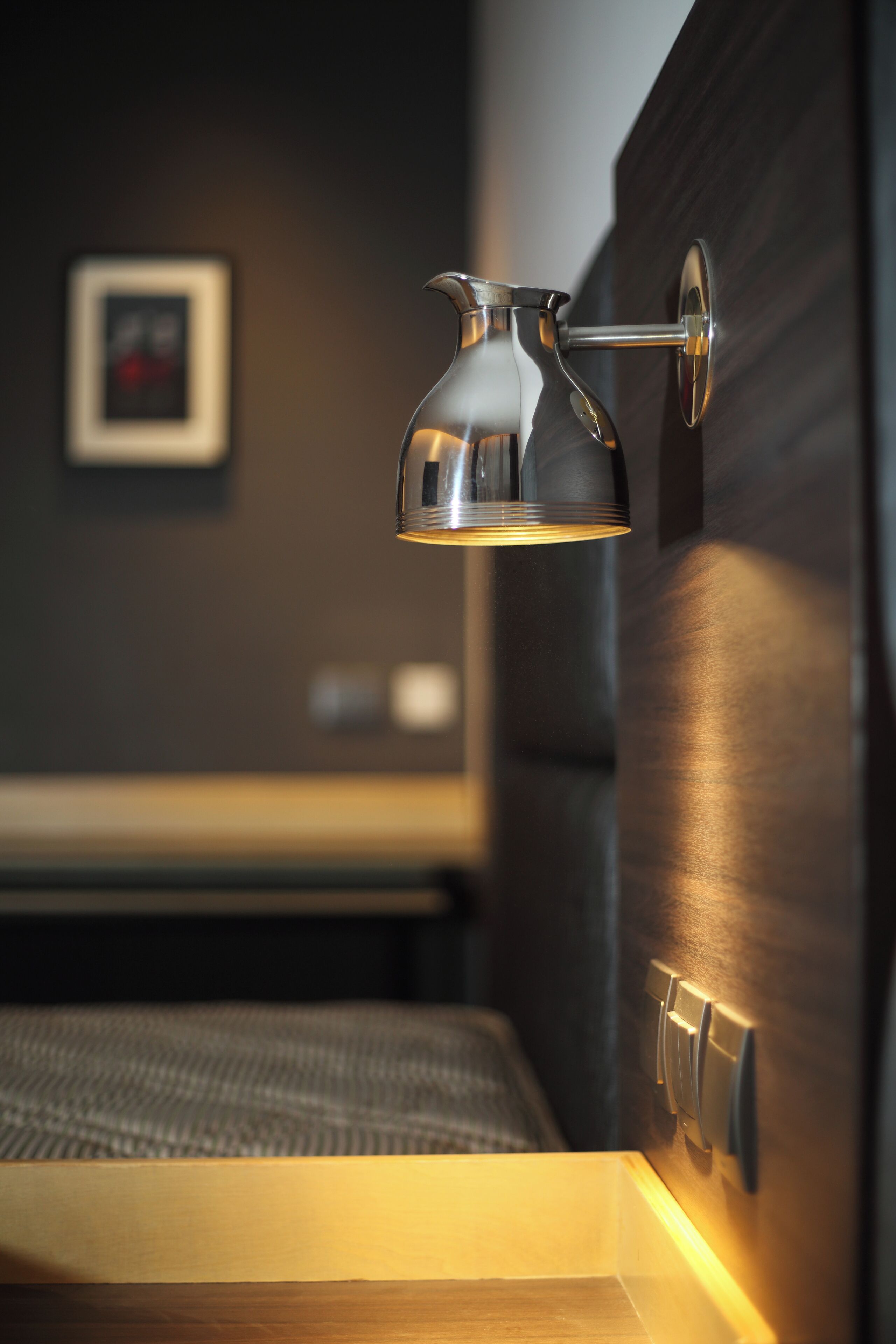 Una habitación moderna con una lámpara de pared, un cuadro enmarcado y una mesita de noche de madera.