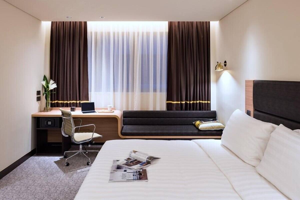 A hotel room with a bed, a desk, a chair, a laptop, and a window with curtains.