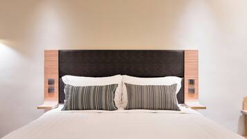 A modern hotel room with a large bed, two pillows, a wooden headboard, and bedside tables with lamps.