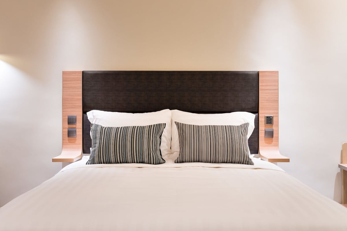 Un letto rifatto con due cuscini, una testata scura e pannelli laterali in legno con illuminazione integrata.