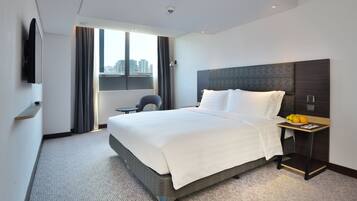 A modern hotel room with a large bed, a bedside table with fruits, a chair, and a city view through the window.