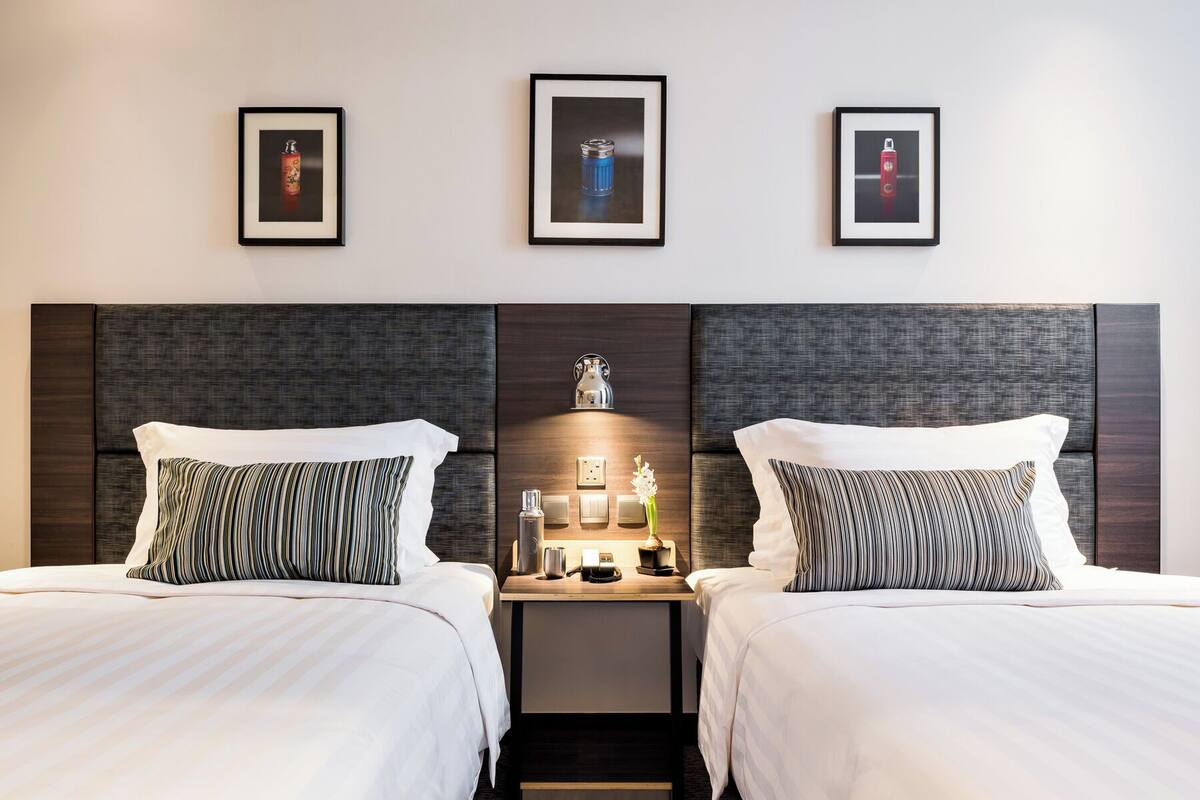 A hotel room with two beds, a nightstand with a lamp, and three framed pictures on the wall.