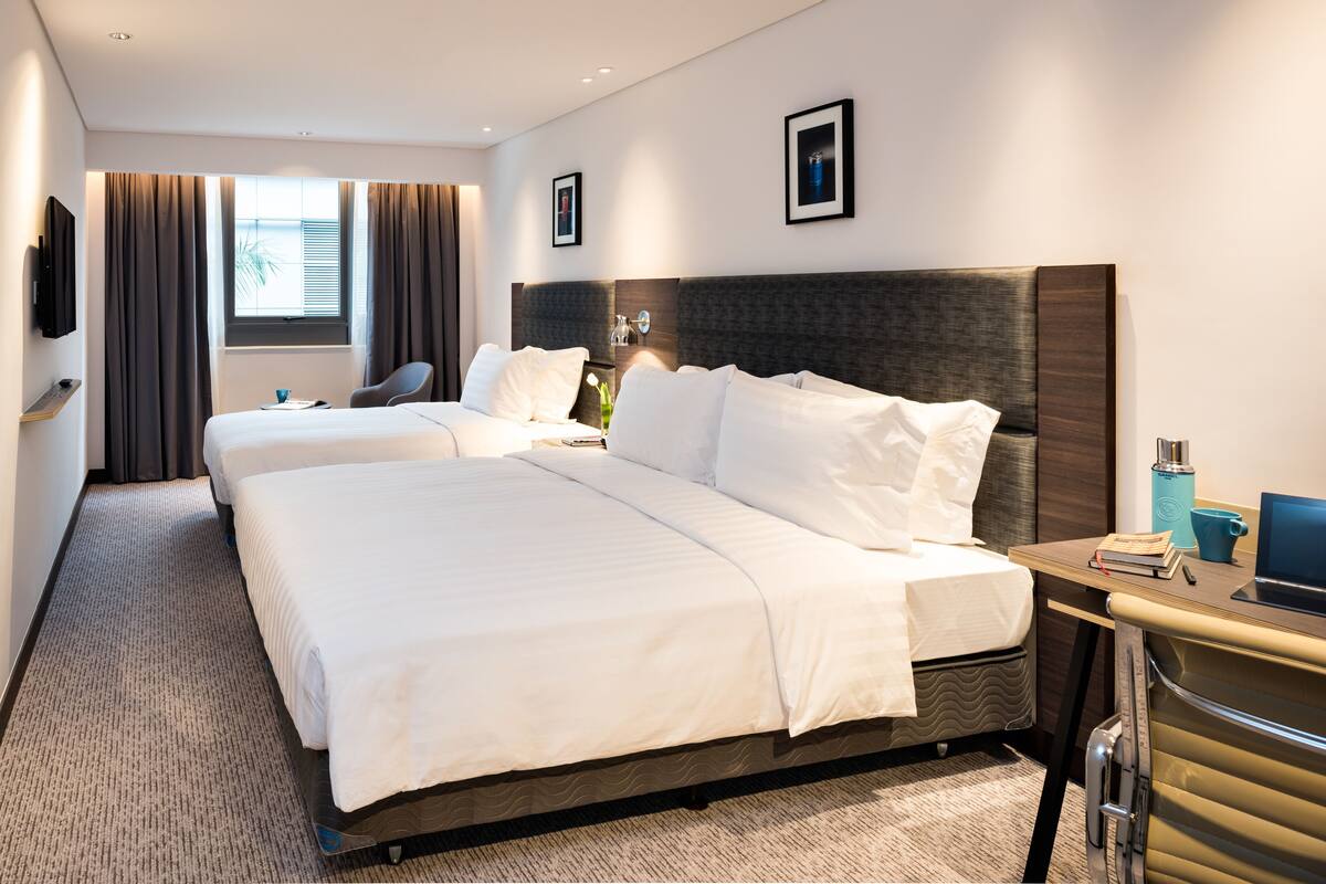 A hotel room with two beds, a desk, a chair, a TV, and a window with curtains.