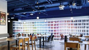 Un café moderno con mobiliario de madera, una pared de botellas de colores y tuberías del techo a la vista.