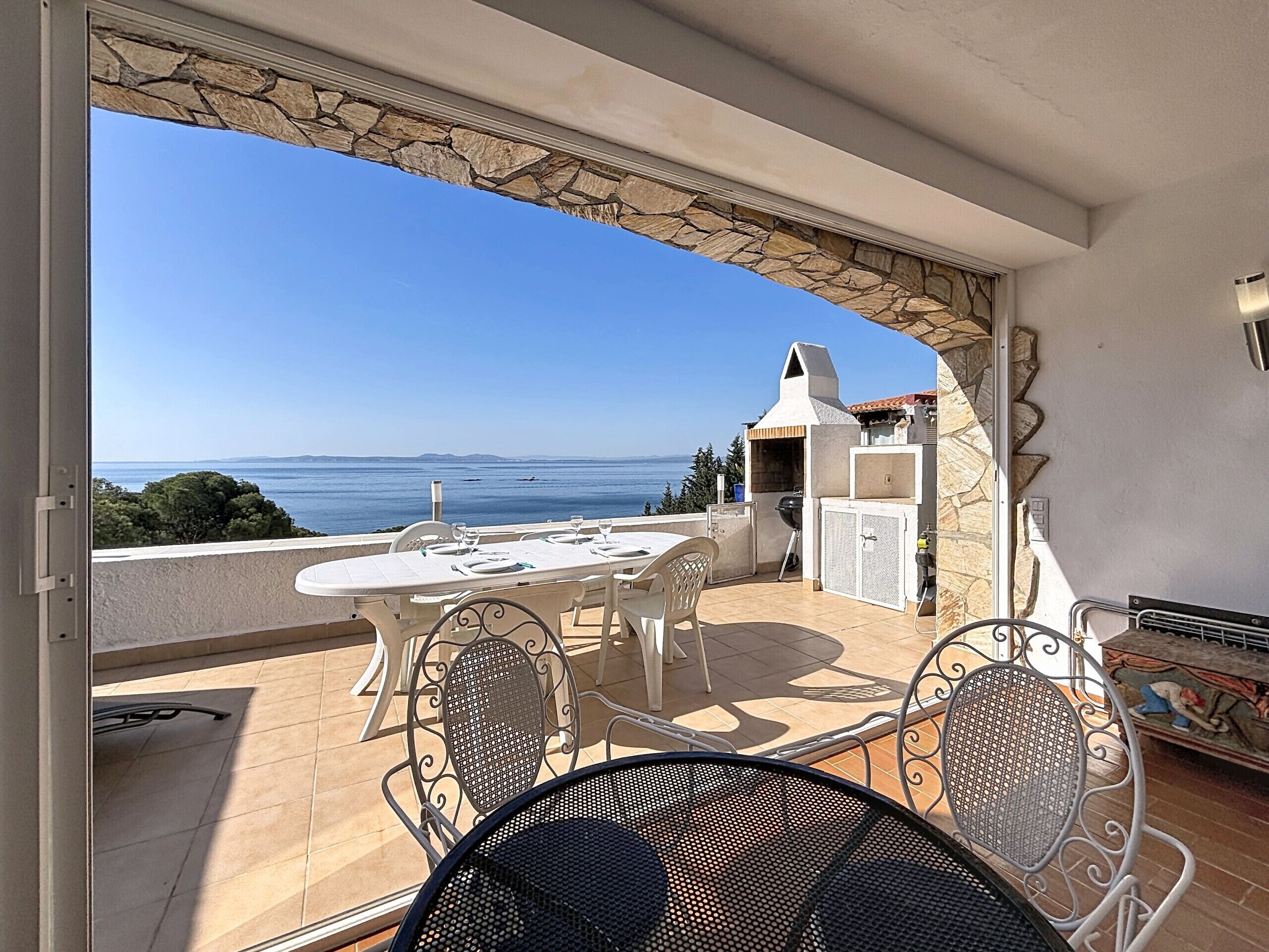Ein Balkon mit Tisch und Stühlen, ein Steinbogen und Meerblick.