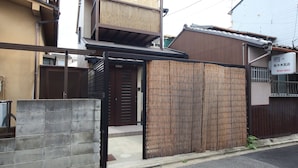 Een traditioneel Japans huis met een houten poort, een betonnen muur en een kleine ingang.