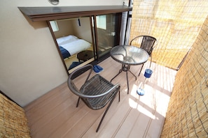 A small balcony with wicker furniture, a glass door leading to a bedroom, and a view of the outside. - Kyo Trust (Kyoto)