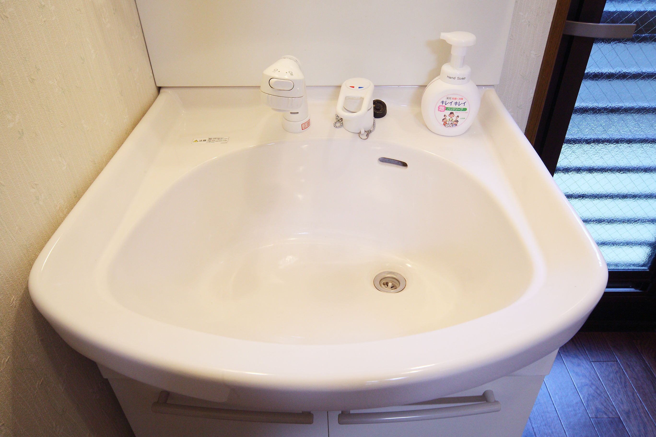 A white bathroom sink with a handheld soap dispenser and a bottle of hand soap.